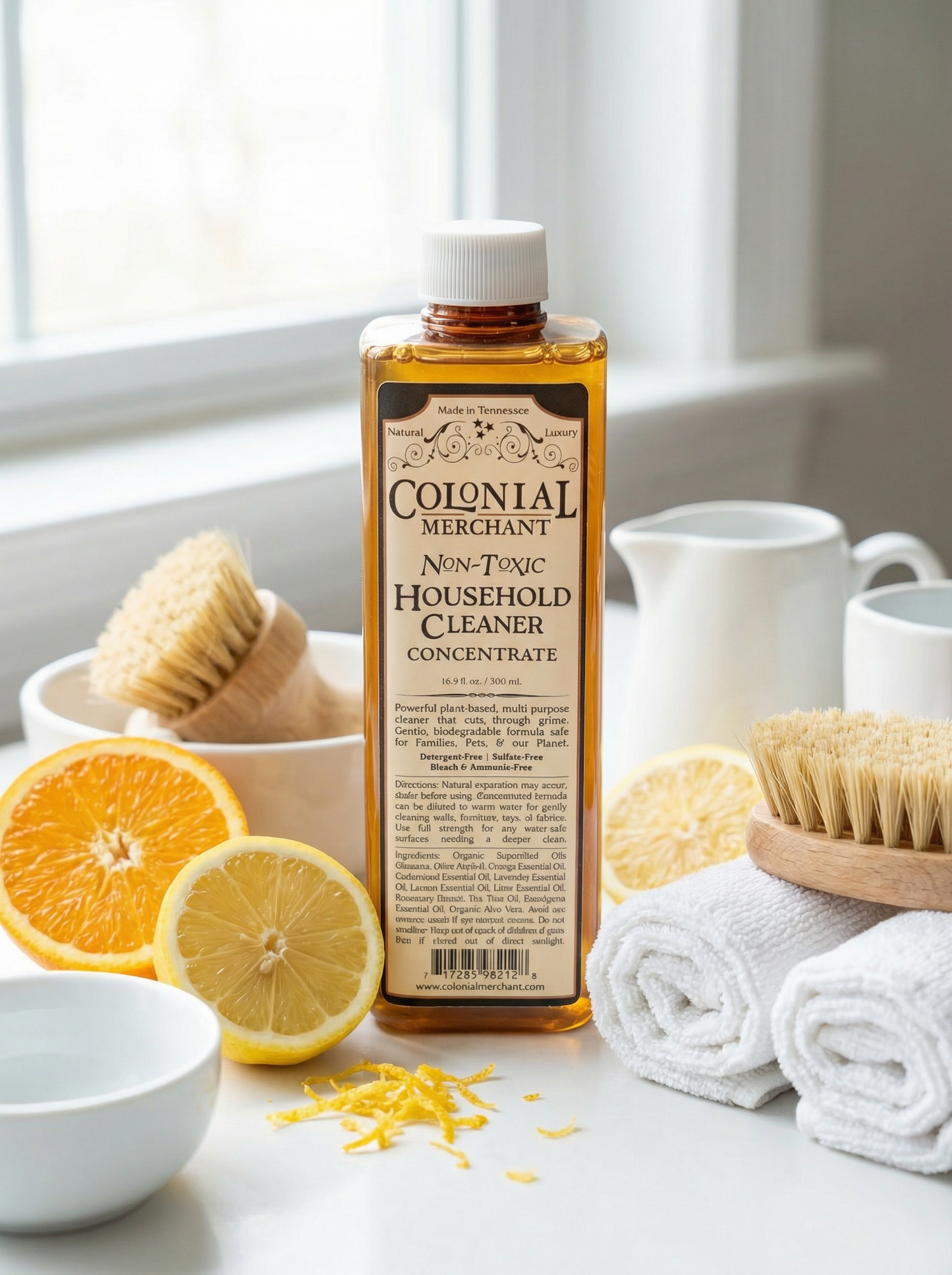 Bottle of Colonial Merchant Non-Toxic Household Cleaner Concentrate with lemons, oranges, and cleaning items on a surface.